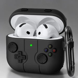 Könnte beinhalten: Schwarze Schutzhülle für kabellose Ohrhörer, im Design eines Videospiel-Controllers. Die Hülle verfügt über ein Steuerkreuz, Tasten und eine grüne Betriebsanzeige. Inklusive schwarzem Karabinerhaken.