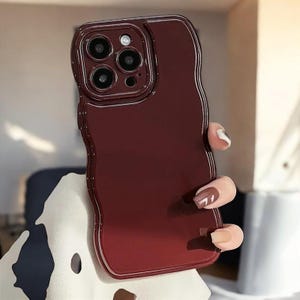 Könnte beinhalten: Eine burgunderrote Handyhülle mit welligem Design und einem erhöhten Kameraobjektiv.