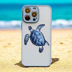 Puede incluir: Una funda de teléfono azul claro con un diseño de tortuga marina. La tortuga es azul y gris y está nadando hacia el lado derecho de la funda. La funda del teléfono tiene un recorte para el objetivo de la cámara con tres círculos negros.