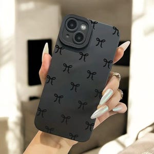 Może przedstawiać: Czarne etui na telefon z powtarzającym się wzorem czarnych kokardek. Etui ma wystający obiektyw aparatu z nadrukowanym tekstem "Pro Camera".