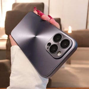 Op de afbeelding: Een zilveren telefoonhoesje met een geborstelde metalen afwerking en een drievoudige camera lens.
