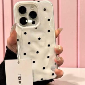Könnte beinhalten: Weißes Handycase mit schwarzen Polka Dots. Das Case hat ein glänzendes Finish und einen Kameraausschnitt. Ein Etikett mit dem Text "INS HO" ist angebracht.