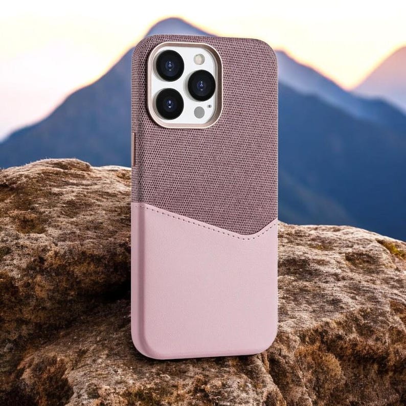 May include: A pink and gray phone case with a textured fabric top and a smooth leather bottom. The case has a cutout for the camera lens.