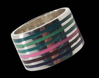 Op de afbeelding: Een zilveren ring met een brede band met meerdere strepen van groene, roze en blauwe inleg.