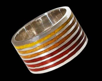 Op de afbeelding: Een zilveren ring met een brede band met meerdere strepen van rood, oranje en geel email.