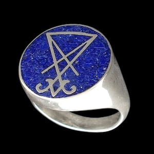 Op de afbeelding: Een zilveren ring met een blauwe lapis lazuli-steen in het midden. De steen is gegraveerd met een zilveren zegel.