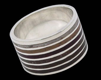 Op de afbeelding: Een zilveren ring met een brede band met meerdere strepen van bruine, zwarte en witte inleg.