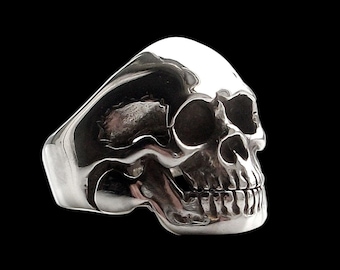 May include: A silver skull ring with a detailed design. The skull is facing to the right and has a prominent jawline.