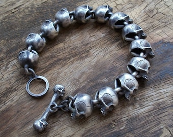 May include: A silver bracelet made of linked skull charms. The bracelet has a silver toggle clasp with a bone design.