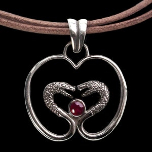 May include: Silver pendant necklace with a heart-shaped design featuring two intertwined snakes with a red gemstone in the center.