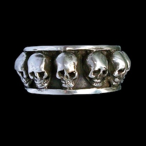 Könnte beinhalten: Ein silberner Ring mit einer Reihe von Totenköpfen. Die Totenköpfe sind alle nach vorne gerichtet und haben ein detailliertes Design.