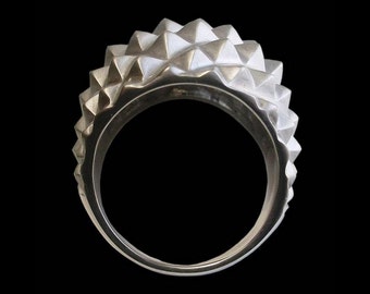 Può includere: Un anello d'argento con un design testurizzato e appuntito. L'anello è in metallo e ha una finitura liscia e lucida.