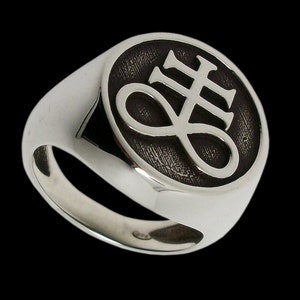 May include: A silver ring with a black oval-shaped setting featuring a white symbol of a cross with an infinity symbol.