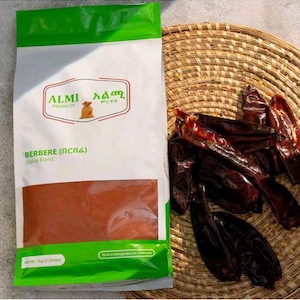 May include: A bag of ALMI Products Berbere spice blend, with a net weight of 1 kg (2.204 lbs). Dried red chili peppers are in a woven basket to the right. The bag is white with green accents and a clear window showing the spice.