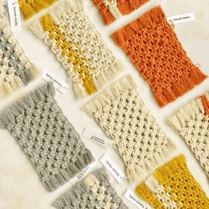 May include: A collection of rectangular macrame coasters featuring intricate knotted patterns and fringed edges. The coasters are available in solid colors including mustard yellow, burnt orange, grey, and cream, with some designs featuring two-tone stripes.