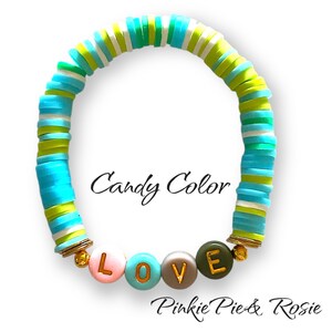 May include: A colourful bracelet made of stacked, round, ceramic beads in shades of blue, green, and white. The bracelet has gold accents and features the word "LOVE" spelled out in larger beads with gold lettering. The bracelet is labelled "Candy Color" and "Pinkie Pie & Rosie".
