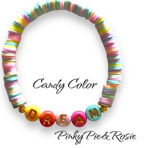 May include: A colourful bracelet made of stacked pastel-coloured beads with the word "DREAM" spelled out in gold letters on larger beads. The bracelet is labelled "Candy Color" and "Pinky Pie & Rosie".