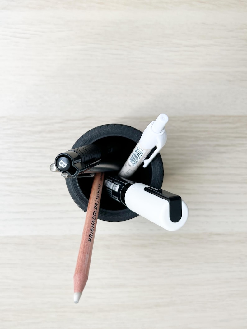 May include: A black pencil holder with a white pen, a black pen, a white marker, and a brown Prismacolor pencil inside.