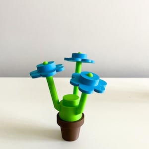 K&ouml;nnte beinhalten: Ein 3D-gedruckter Blumentopf mit drei blauen Bl&uuml;ten und gr&uuml;nen Stielen. Der Topf ist braun und die Bl&uuml;ten sind mit einer gr&uuml;nen Basis an den Stielen befestigt.