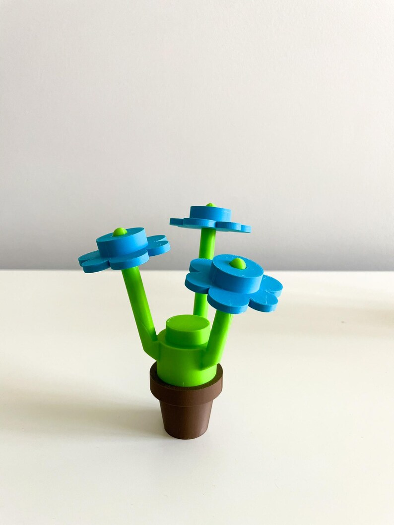K&ouml;nnte beinhalten: Ein 3D-gedruckter Blumentopf mit drei blauen Bl&uuml;ten und gr&uuml;nen Stielen. Der Topf ist braun und die Bl&uuml;ten sind mit einer gr&uuml;nen Basis an den Stielen befestigt.