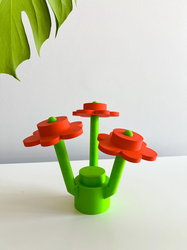 K&ouml;nnte beinhalten: Eine dreidimensionale Skulptur einer Blumenarrangements mit drei roten Blumen und gr&uuml;nen Stielen. Die Blumen haben eine abgerundete Mitte und f&uuml;nf Bl&uuml;tenbl&auml;tter. Die Stiele sind mit einer gr&uuml;nen Basis verbunden.