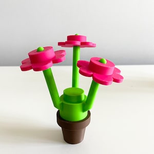 K&ouml;nnte beinhalten: Eine kleine Topfpflanze mit drei rosa Bl&uuml;ten und gr&uuml;nen Stielen. Der Topf ist braun und die Pflanze ist aus Plastik.