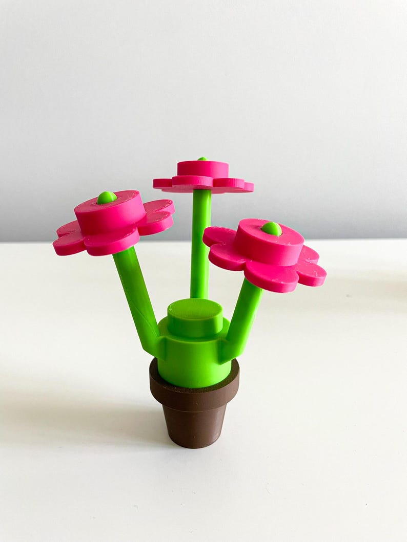 K&ouml;nnte beinhalten: Eine kleine Topfpflanze mit drei rosa Bl&uuml;ten und gr&uuml;nen Stielen. Der Topf ist braun und die Pflanze ist aus Plastik.