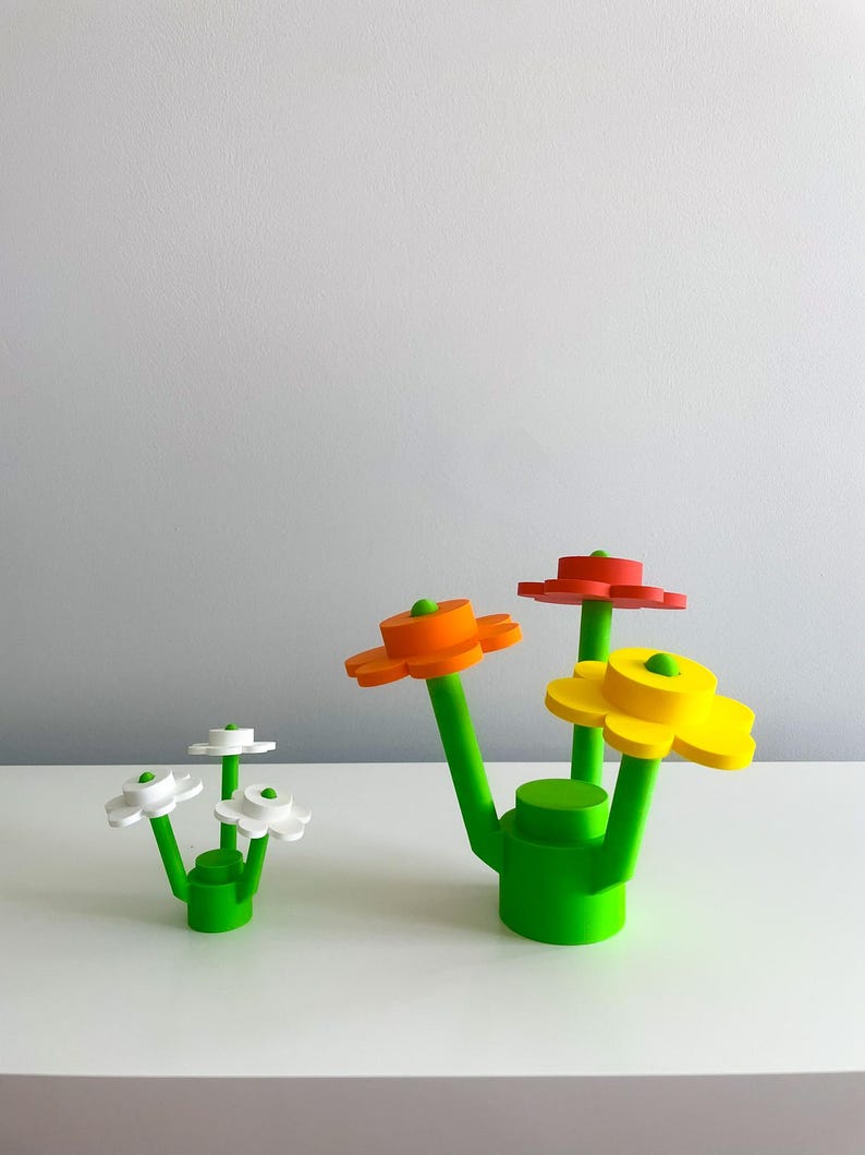 K&ouml;nnte beinhalten: Drei bunte Blumenskulpturen aus Kunststoff. Die Blumen sind rot, orange und gelb. Die Stiele sind gr&uuml;n und die Basis ist gr&uuml;n. Die Blumen sind in einer Gruppe angeordnet.