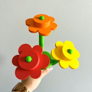 K&ouml;nnte beinhalten: Drei farbenfrohe, blumenf&ouml;rmige Objekte mit gr&uuml;nen Stielen. Die Blumen sind orange, rot und gelb.