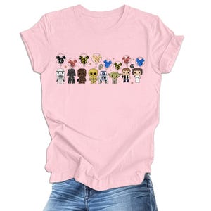 Pode incluir: Camiseta rosa com um gr&aacute;fico de personagens de Star Wars segurando bal&otilde;es. Os personagens incluem Darth Vader, R2-D2, Chewbacca, Yoda e outros.