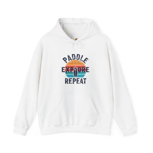 May include: White hoodie with a vintage-style graphic that says "Paddle Explore Repeat" with a sunset and surfboard design.