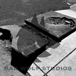 May include: A black and white photo of a cracked sidewalk with a metal grate covering a utility access point. The grate has a circular design with a hole in the center. The text "Irregular" is visible on the sidewalk.