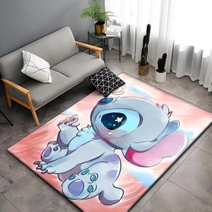 以下が含まれることがあります： リロ＆スティッチのスティッチが描かれたピンクとブルーの漫画の敷物。スティッチは、大きな目とピンクの耳を持つ青い宇宙人です。敷物は水彩画のような背景になっています。