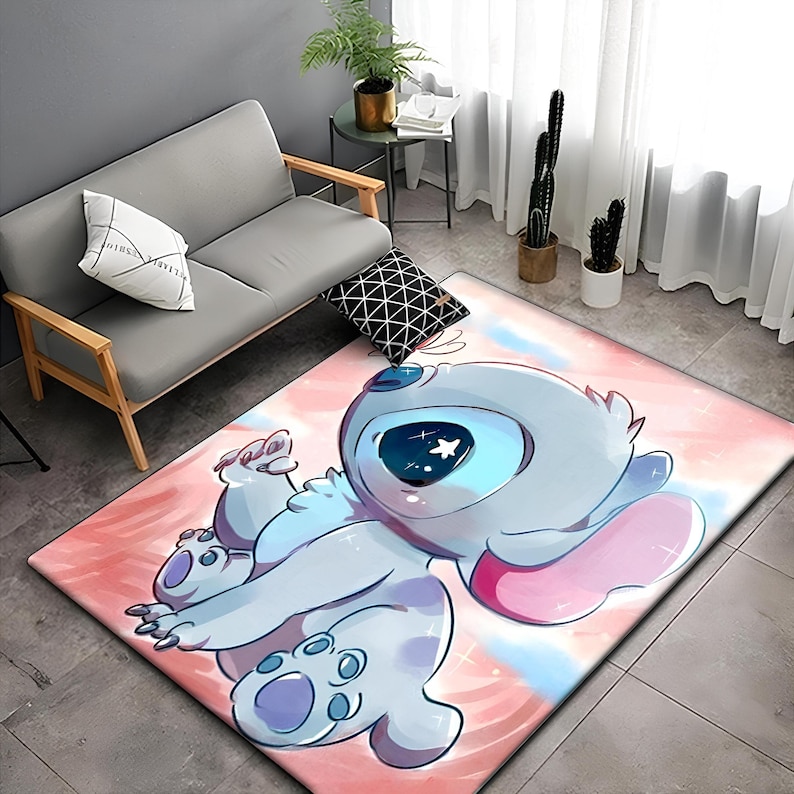 以下が含まれることがあります： リロ＆スティッチのスティッチが描かれたピンクとブルーの漫画の敷物。スティッチは、大きな目とピンクの耳を持つ青い宇宙人です。敷物は水彩画のような背景になっています。