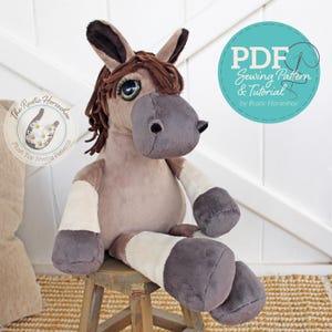 May include: A plush horse toy with a light brown body, dark brown mane and ears, and gray accents. The toy is sitting on a small wooden stool. The image includes text that says "PDF Sewing Pattern & Tutorial by Rustic Horseshoe."