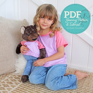 May include: A girl wearing a pink and purple t-shirt and blue jeans is holding a brown teddy bear wearing a purple t-shirt and blue jeans. The image has a text overlay that says "PDF Sewing Pattern & Tutorial by Rustic Horseshoe".