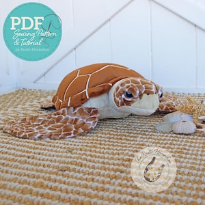 Puede incluir: Un peluche de tortuga marina con caparazón marrón y detalles crema. La tortuga está sobre una estera tejida. La imagen incluye el texto "PDF Sewing Pattern & Tutorial by Rustic Horseshoe."