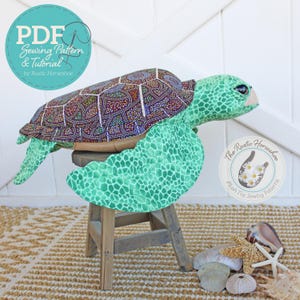 May include: A plush turtle toy with a patterned shell and green flippers sits on a small wooden stool. The turtle's shell features a colorful design. The image includes text that says "PDF Sewing Pattern & Tutorial by Rustic Horseshoe."