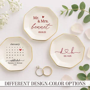 May include: Three octagonal, off-white ring dishes with gold rims. One dish has a calendar design with a heart on a date, another has the initials "d&h", and the third says "Mr. & Mrs. bennet". Two rings are in front.