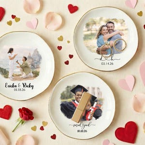 Puede incluir: Tres platos redondos de cer&aacute;mica blanca con bordes dorados, cada uno con una fotograf&iacute;a. Uno muestra una propuesta de matrimonio, otro una pareja abraz&aacute;ndose y el tercero un graduado. Corazones decorativos y p&eacute;talos de rosa rodean los platos.