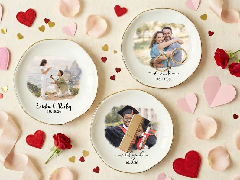 Puede incluir: Tres platos redondos de cer&aacute;mica blanca con bordes dorados, cada uno con una fotograf&iacute;a. Uno muestra una propuesta de matrimonio, otro una pareja abraz&aacute;ndose y el tercero un graduado. Corazones decorativos y p&eacute;talos de rosa rodean los platos.