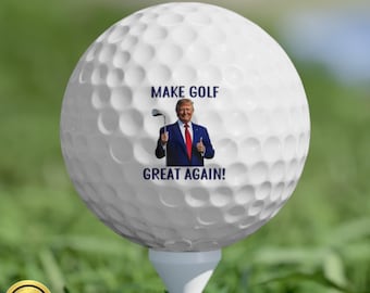 May include: White golf ball with a printed image of a man in a suit holding a golf club. The text "MAKE GOLF GREAT AGAIN!" is printed on the ball.