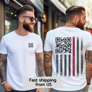 Op de afbeelding: Wit T-shirt met een QR-code op de voorkant en een versleten vlagontwerp op de achterkant. Het vlagontwerp heeft zwarte en grijze strepen met een rode streep.