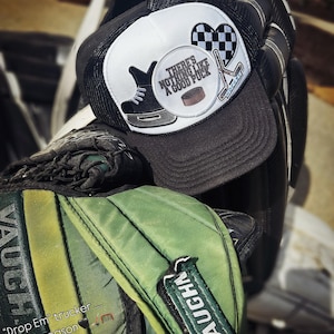 May include: A black and white trucker hat with a hockey-themed patch that says "There's nothing like a good puck." The hat is sitting on top of a green hockey bag with the word "Vaughn" written on it.