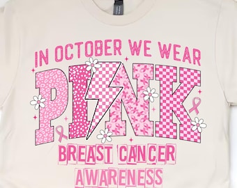 Könnte beinhalten: Cremefarbenes T-Shirt mit dem Text "IN OCTOBER WE WEAR PINK BREAST CANCER AWARENESS" in Rosa. Das Wort "PINK" ist mit einem Blitz und floralen Akzenten versehen. Das Shirt hat einen Rundhalsausschnitt.