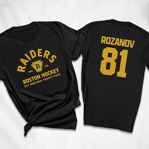 May include: Black t-shirts with gold lettering. One shirt displays "RAIDERS BOSTON HOCKEY EST. NINETEEN TWENTY-FOUR" and a logo. The other shirt has "ROZANOV 81" on the back. Both shirts are short-sleeved.