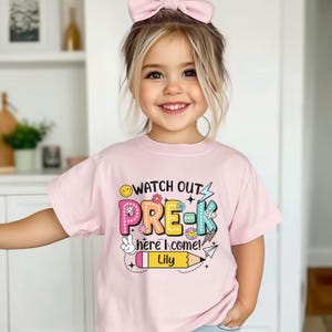May include: A light pink short-sleeved t-shirt with the words "WATCH OUT PRE-K here I come!" in colorful letters. The shirt also features a pencil with the name "Lily".