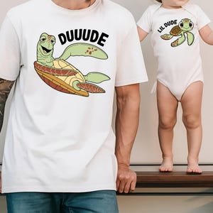 May include: White t-shirt with a cartoon turtle graphic and the word "DUUUDE" in black. A matching white baby onesie with a turtle graphic and the words "LIL DUDE".