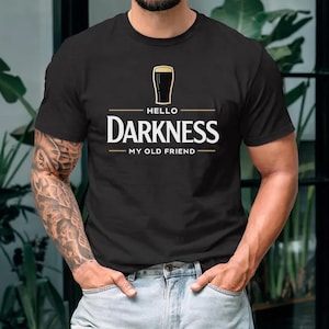 May include: Black t-shirt with the text "Hello Darkness My Old Friend" in white and gold. The design includes a graphic of a pint of beer. The shirt is a classic crew neck style.