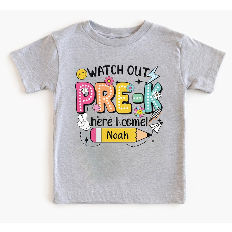 May include: A gray short-sleeved t-shirt with the words "WATCH OUT PRE-K here I come!" in colorful letters and graphics. The name "Noah" is printed on a yellow pencil graphic. The shirt is designed for preschool.